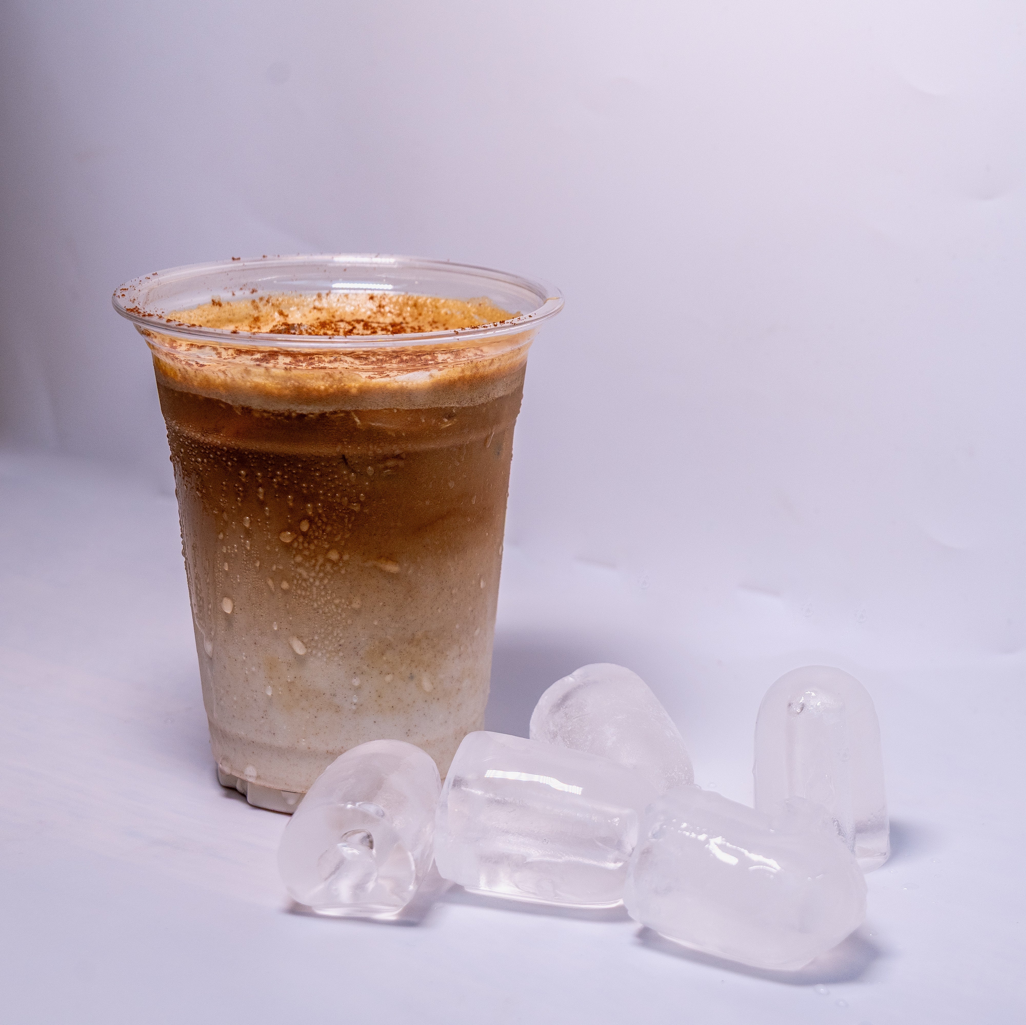 Clear plastic cup with iced coffee and ice cubes on a light gray background
